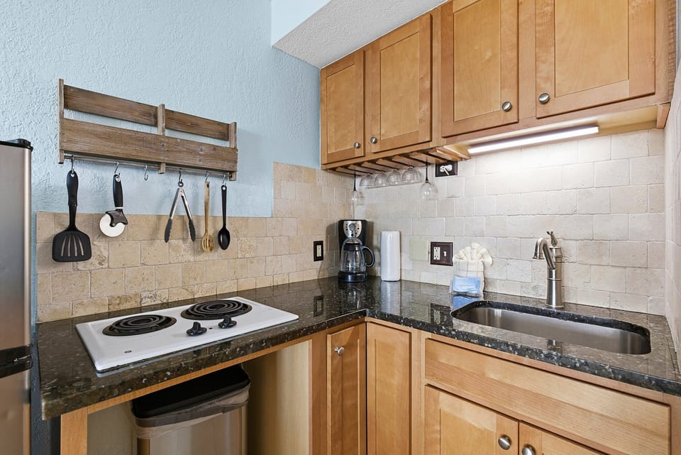 This beach stay studio features a convenient kitchenette with cooktop, sink, coffee maker, and essentials for easy meals. Perfect for fueling up before the beach or relaxing with dinner after a sunny seaside day.