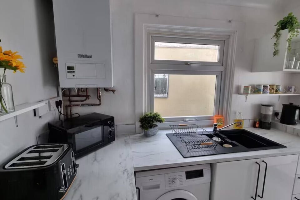 Kitchen area showing a hob, washing machine, and wall-mounted boiler unit, with yellow flowers placed on the counter.