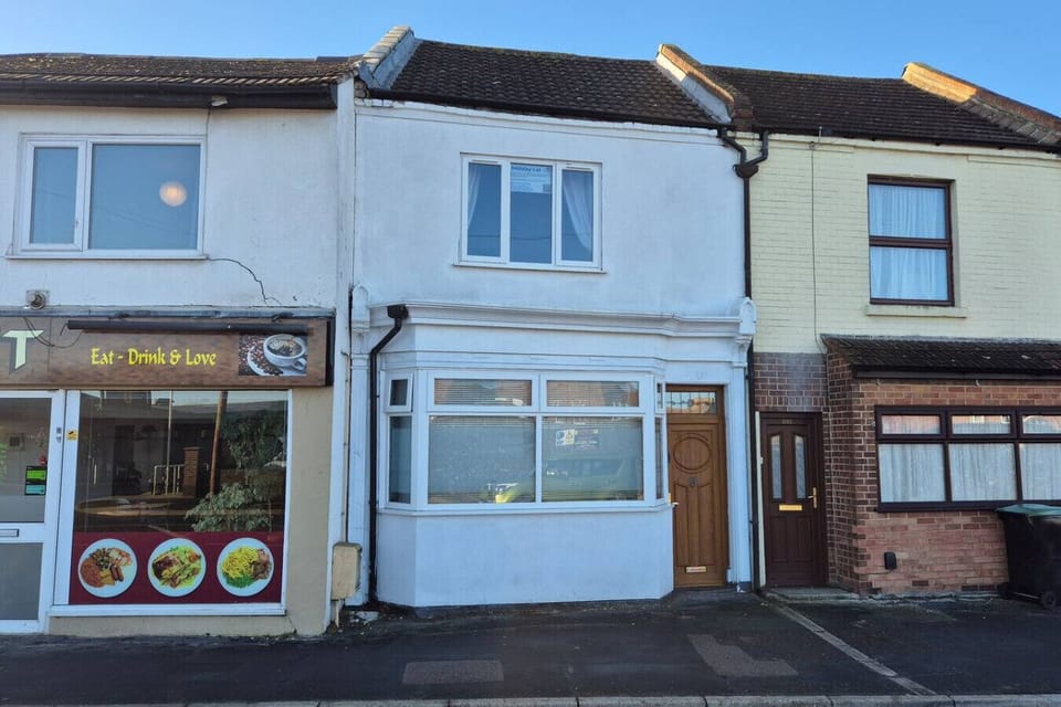 Mid-terrace townhouse exterior with white-painted render, sash-style windows, and a commercial premises visible to the left.