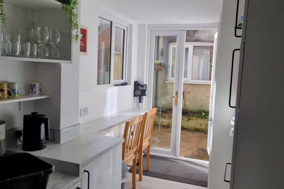 Kitchen and dining area showing a counter with appliances, open shelving with glassware, and a glazed rear door.