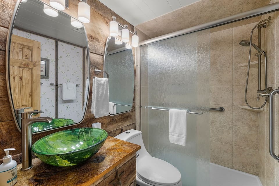Refresh in your spa-inspired bathroom featuring a stunning emerald glass vessel sink and spacious walk-in shower with modern fixtures.