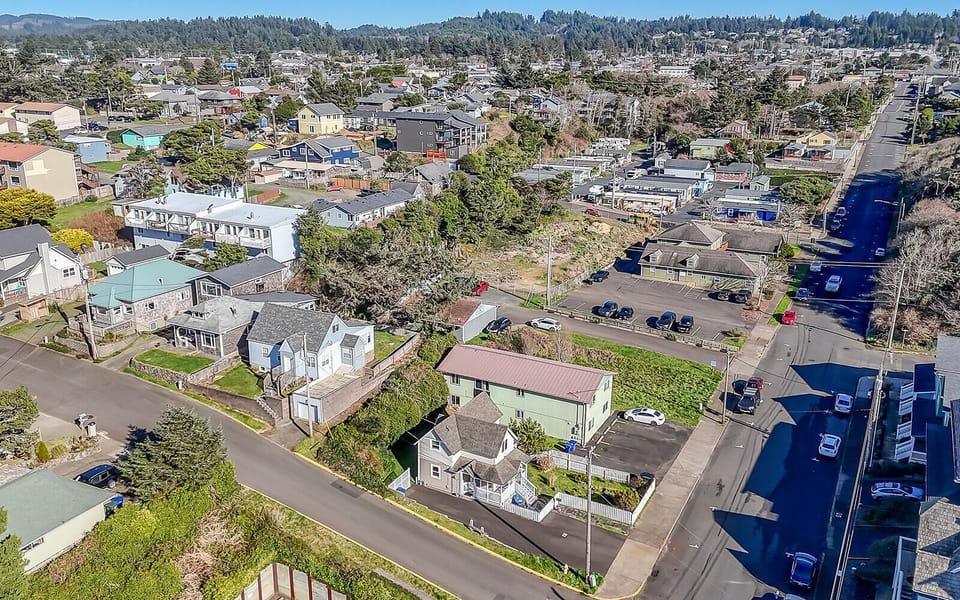 Aerial view of a charming coastal community nestled among forested hills, showcasing the peaceful neighborhood surrounding this property.