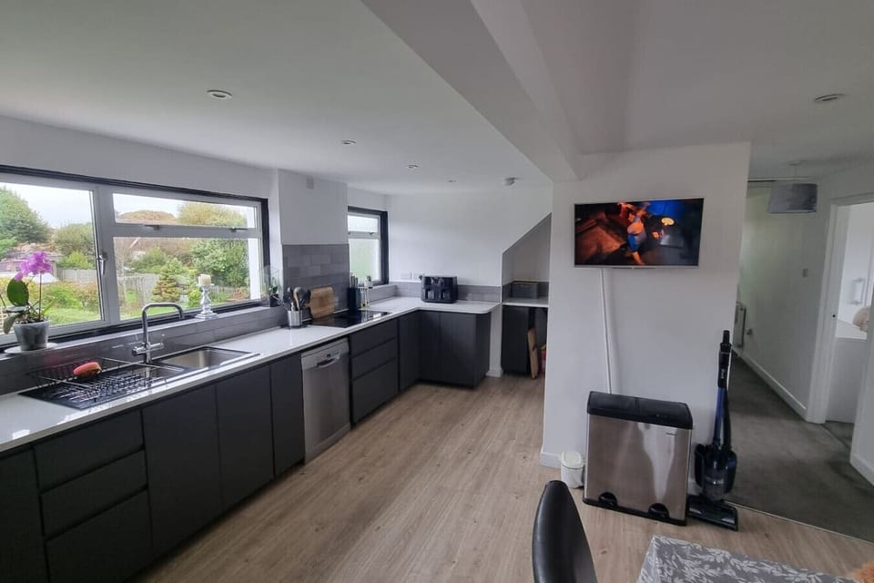 A long, modern kitchen with grey cabinets, wide worktops, and a wall-mounted TV.
