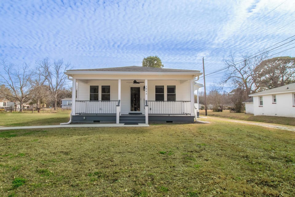 Charming white cottage with welcoming front porch sits on spacious grounds in peaceful residential neighborhood.