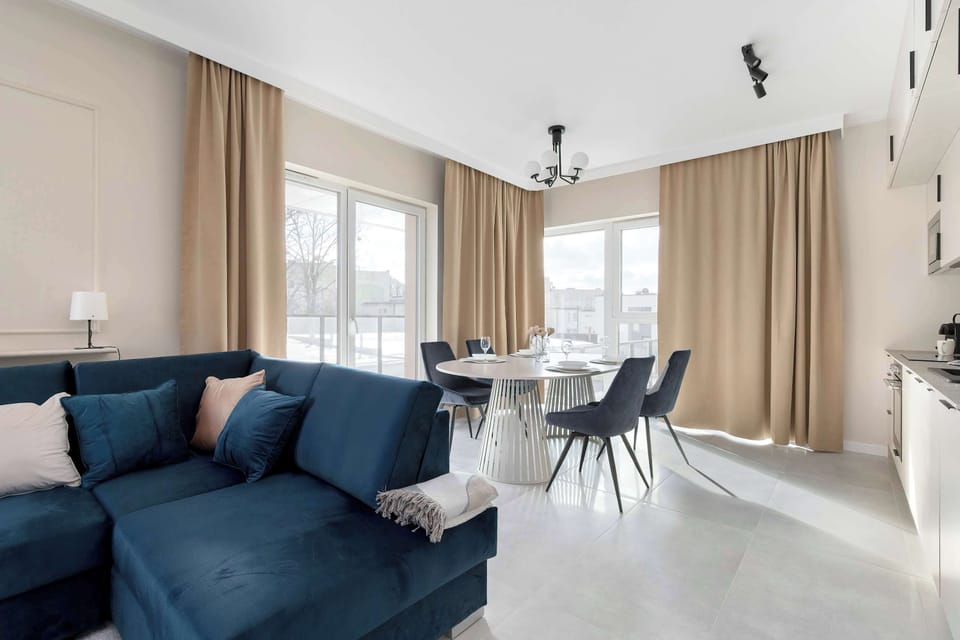 An open-concept living space seamlessly connects the lounge area with the dining section, all framed by elegant floor-to-ceiling curtains. The minimalist design and neutral color palette create an airy and sophisticated atmosphere.