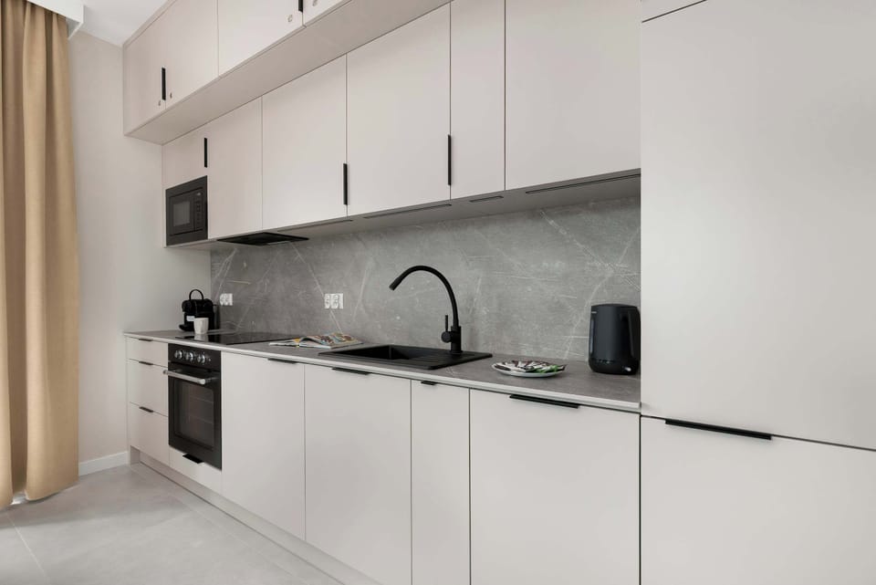 The sleek kitchenette suite is equipped with modern built-in appliances, including an oven and a black induction hob. White cabinetry and a minimalist black faucet create a clean, high-end culinary environment.