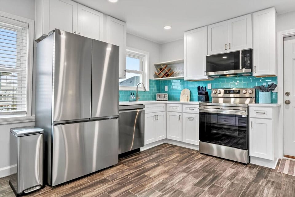 This sleek, modern kitchen features stainless steel appliances, white cabinetry, and a stunning turquoise tile backsplash.