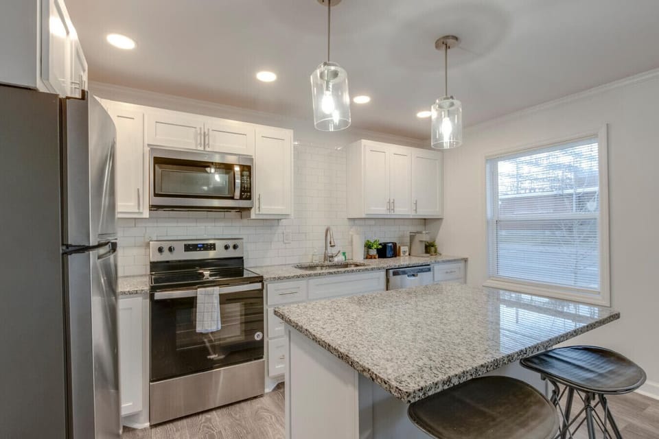 Kitchen from a different angle showing a bright window, pendant lights, and stainless steel appliances