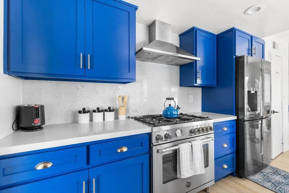 Modern gas range and blue cabinets with a white backsplash for a fresh stainless steel style.