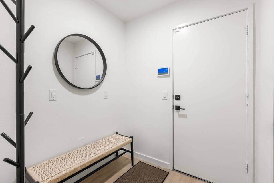 This bright entry features a stylish woven bench, chic mirror, and a modern smart lock.