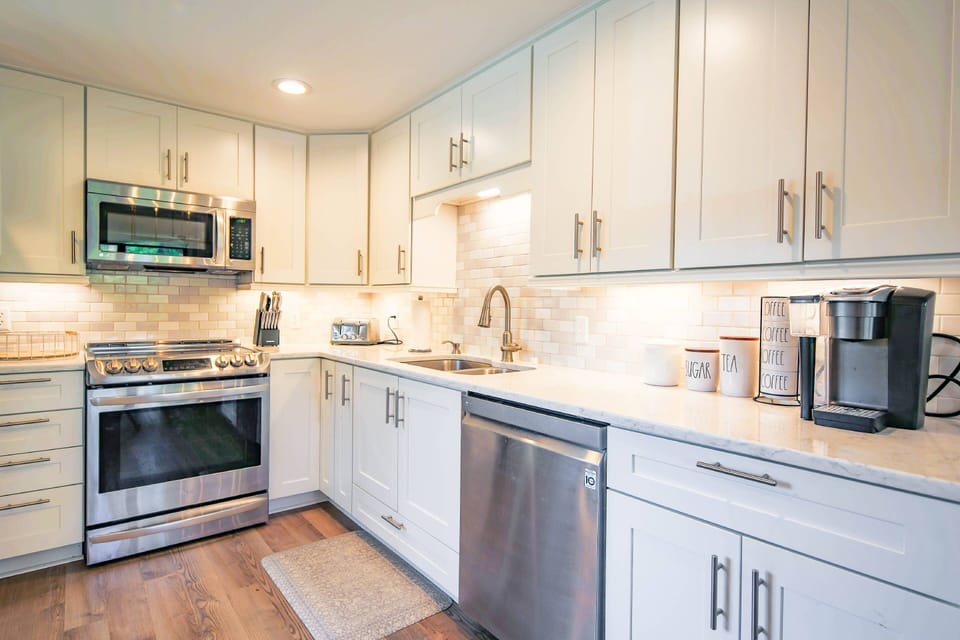 This gorgeous kitchen features white cabinetry, stainless steel appliances and a tiled backsplash.