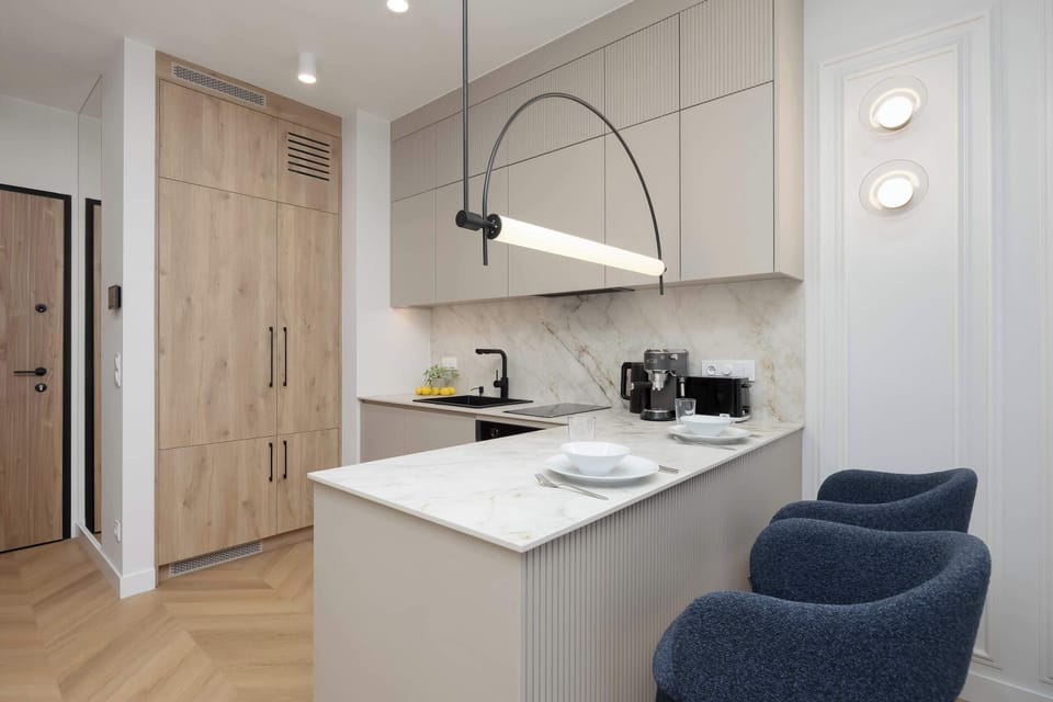 A functional kitchen island topped with white marble, featuring a minimalist black arched light fixture and paired with navy blue chairs.