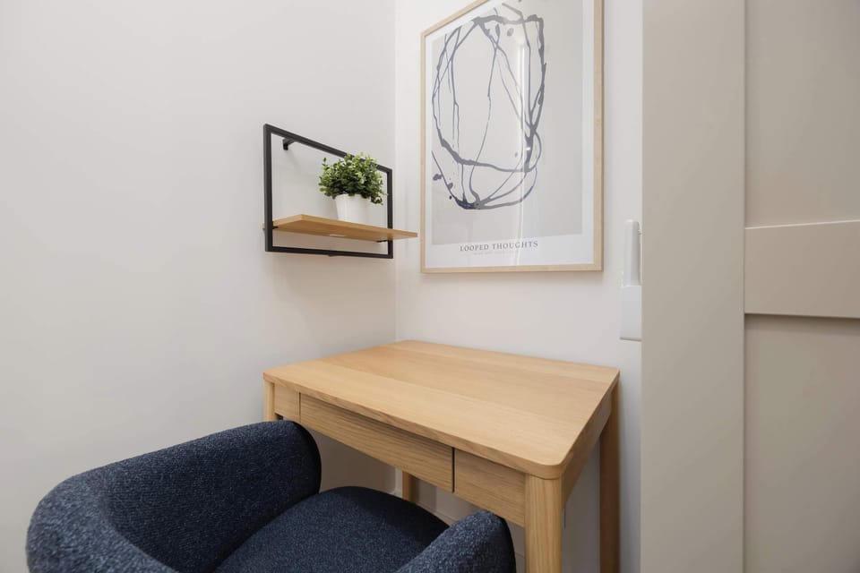 A dedicated home office nook featuring a light wood desk, a navy blue velvet chair, and a minimalist line art piece on the wall.