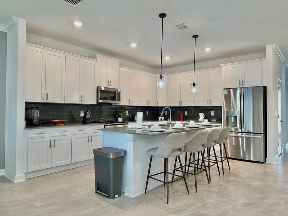 Your sleek kitchen features modern white cabinets, stainless steel appliances, and a spacious island with bar seating perfect for morning coffee.