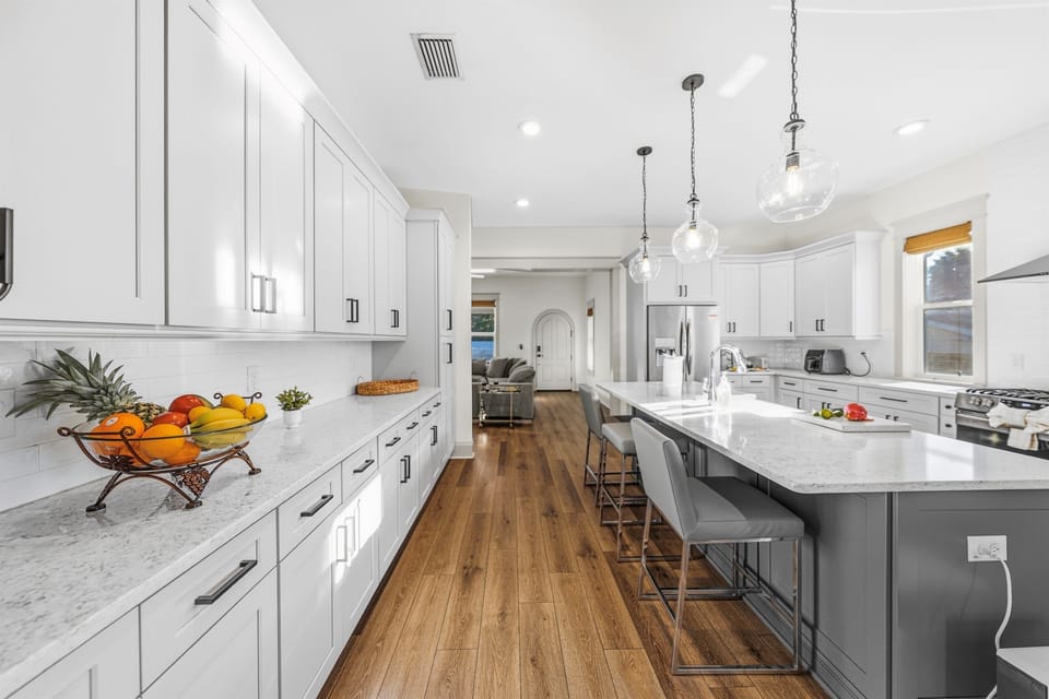 Brand-new kitchen island with pristine white quartz counters, a bowl of fresh tropical fruit, and designer pendant lighting above. Every detail in this Seminole Heights kitchen was chosen with style and function in mind.