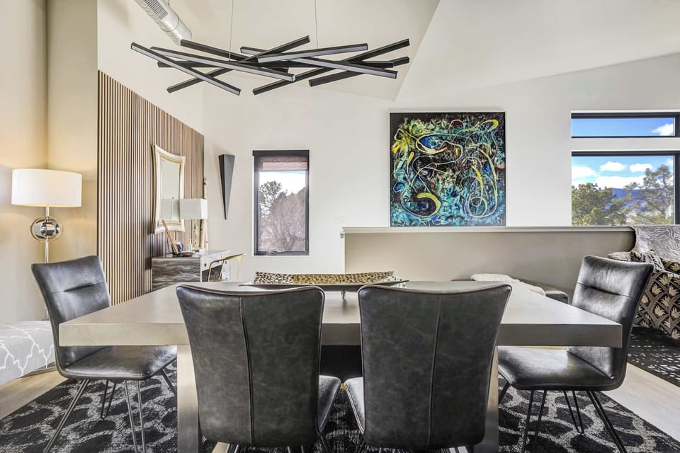 The dining area is defined by a striking geometric area rug and a sculptural light fixture. Vertical wood slat accents bring warmth to the contemporary design, creating an inviting space for shared meals and conversation.