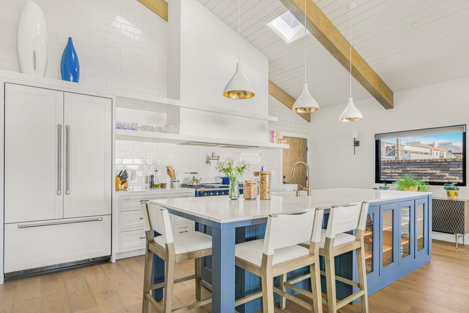 A bright, modern kitchen with white cabinetry, a large blue island, and vaulted ceilings with exposed beams.