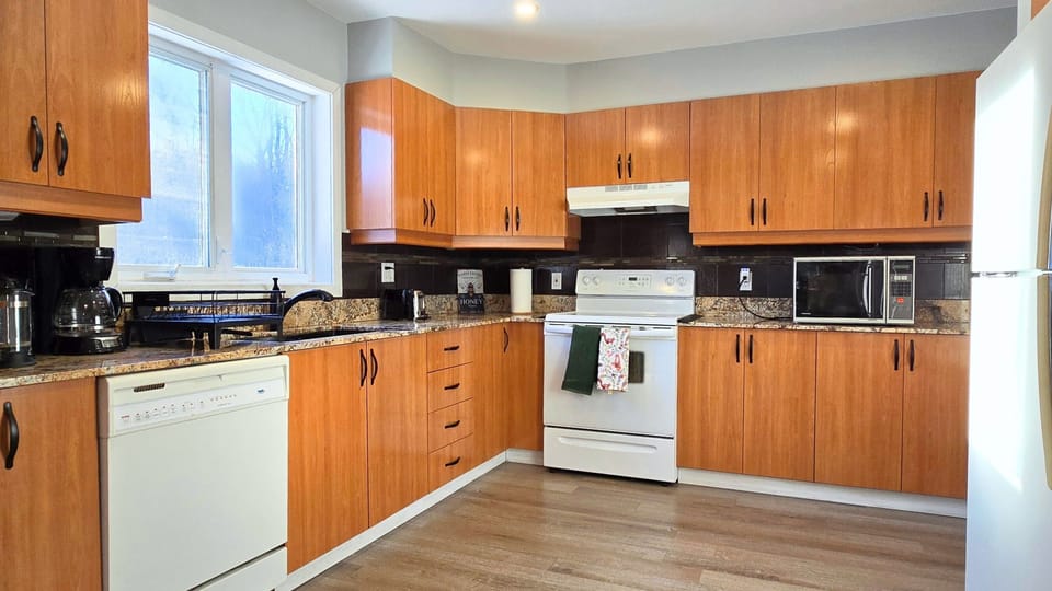Fully-equipped kitchen with fridge, stove, microwave, dishwasher, dishware.