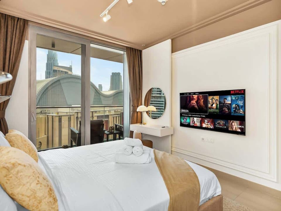 The bedroom offers Burj Khalifa views from the window, direct access to the balcony, a wall-mounted smart TV, and a built-in vanity that doubles as a functional workspace.