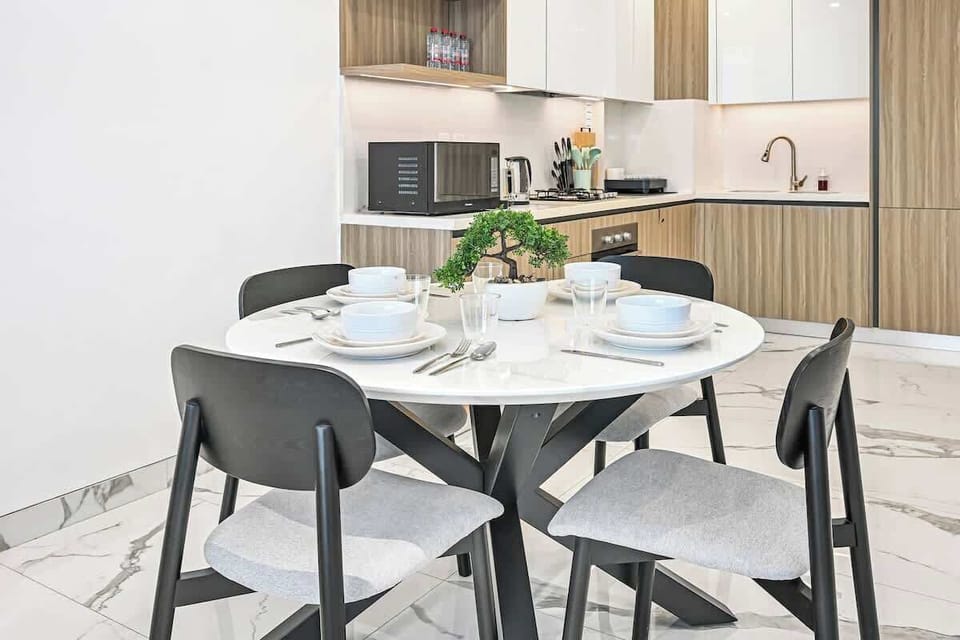 Enjoy meals at a stylish round dining table with seating for four. Perfect for both casual dining and relaxed conversations, set against a modern open kitchen.