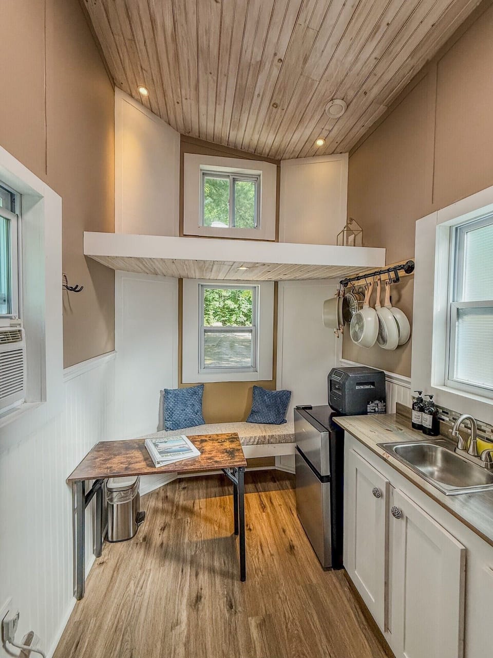 Bright tiny home kitchen with loft, dining nook, and rustic wood ceiling