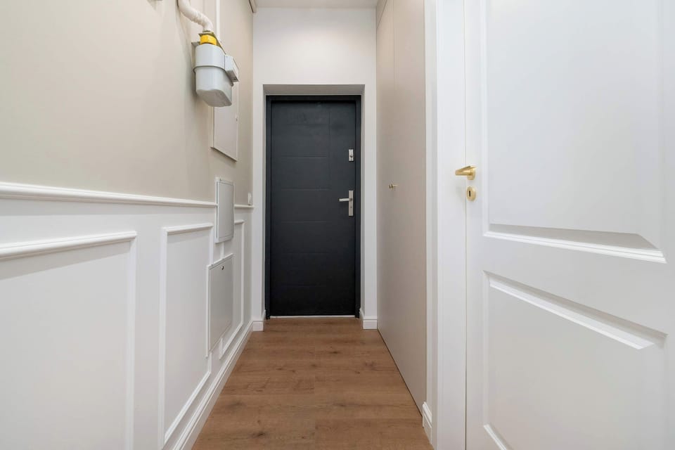 The entrance hallway is bright and welcoming, featuring white wall paneling and a dark, sturdy front door. The wooden flooring continues through the corridor, leading into the main living areas.