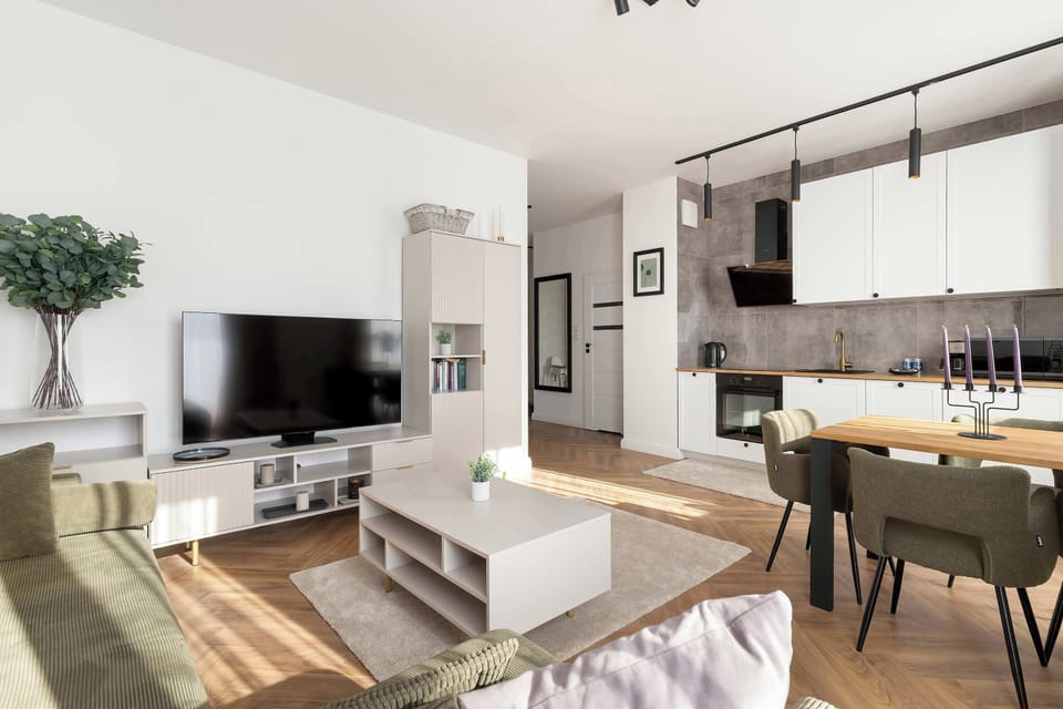 An open-plan living room and kitchenette area with a dining table in the background. The layout feels airy and functional with coordinated furniture and decor.