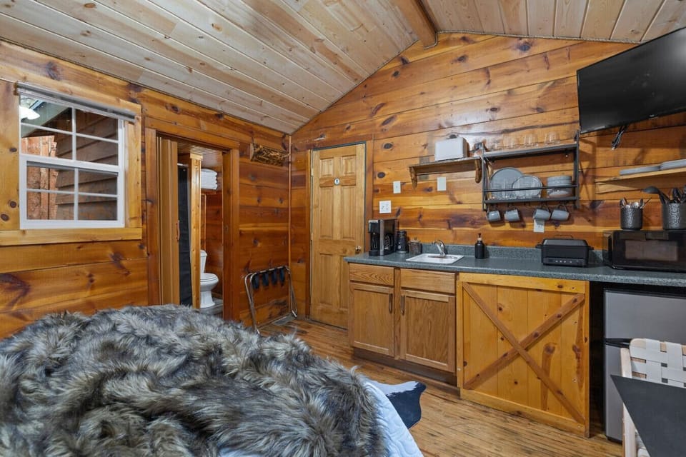 Spacious and inviting studio featuring a comfortable queen bed, a fully equipped kitchen for all your cooking needs, and charming log cabin details that add warmth and character.
