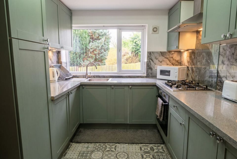 A sage-green fitted kitchen with stone worktops and a garden-facing window to cook by.
