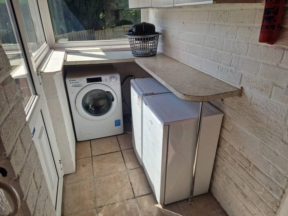 Laundry area housing a washing machine and an additional white appliance on a tiled floor beside a window.