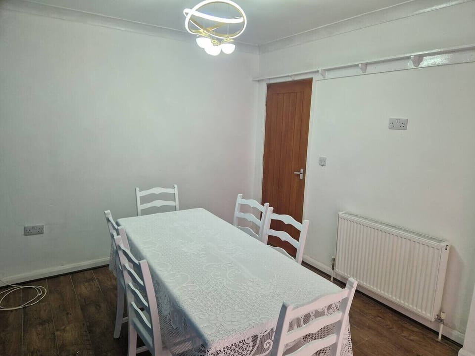 Dining area with a white rectangular table and four white chairs, a radiator, and laminate flooring