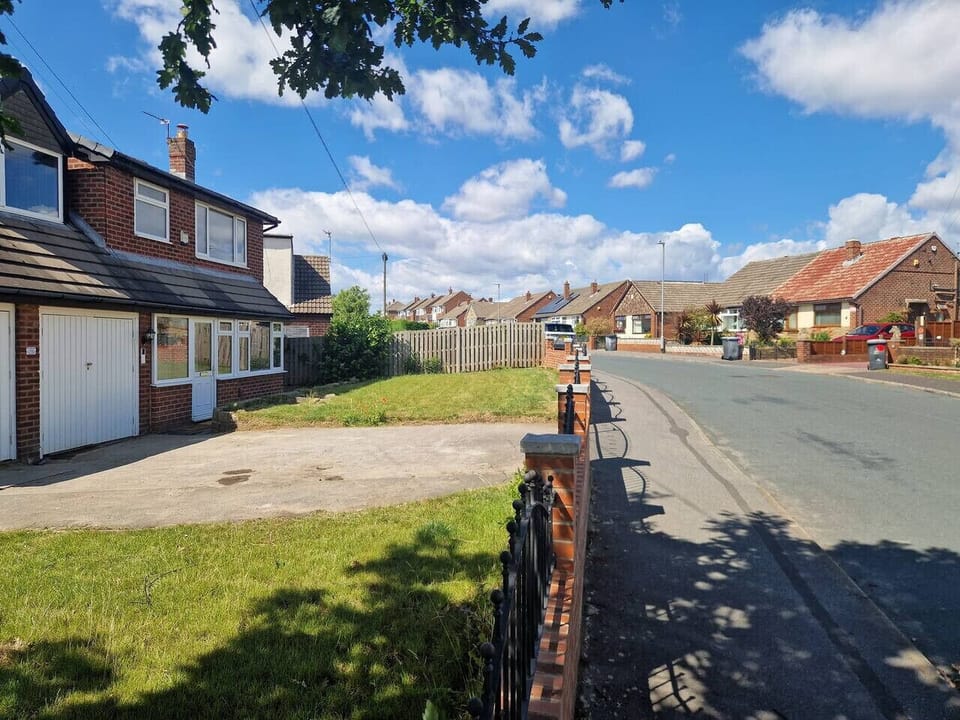 Front elevation of the property showing the driveway, front garden, and adjacent street on a sunny day.