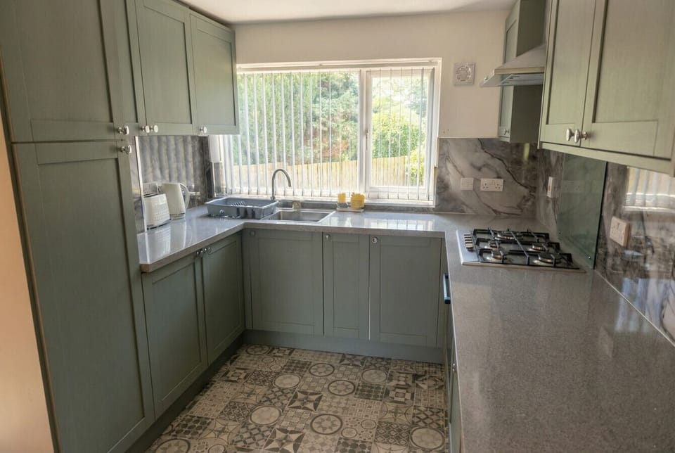 Sage-green units and patterned tiles frame a bright garden-view window in the kitchen.