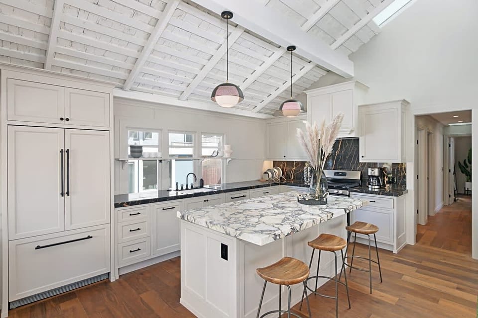 Cook in style in this modern kitchen. It features a marble island with seating, high-end appliances, and beautiful ceilings.