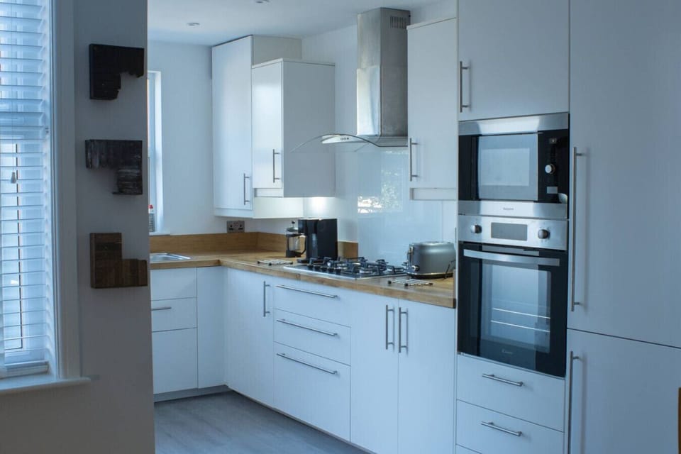 Kitchen units with a built-in oven, combination microwave, extractor hood, and oak-effect worktops, photographed from the opposite end of the kitchen run.