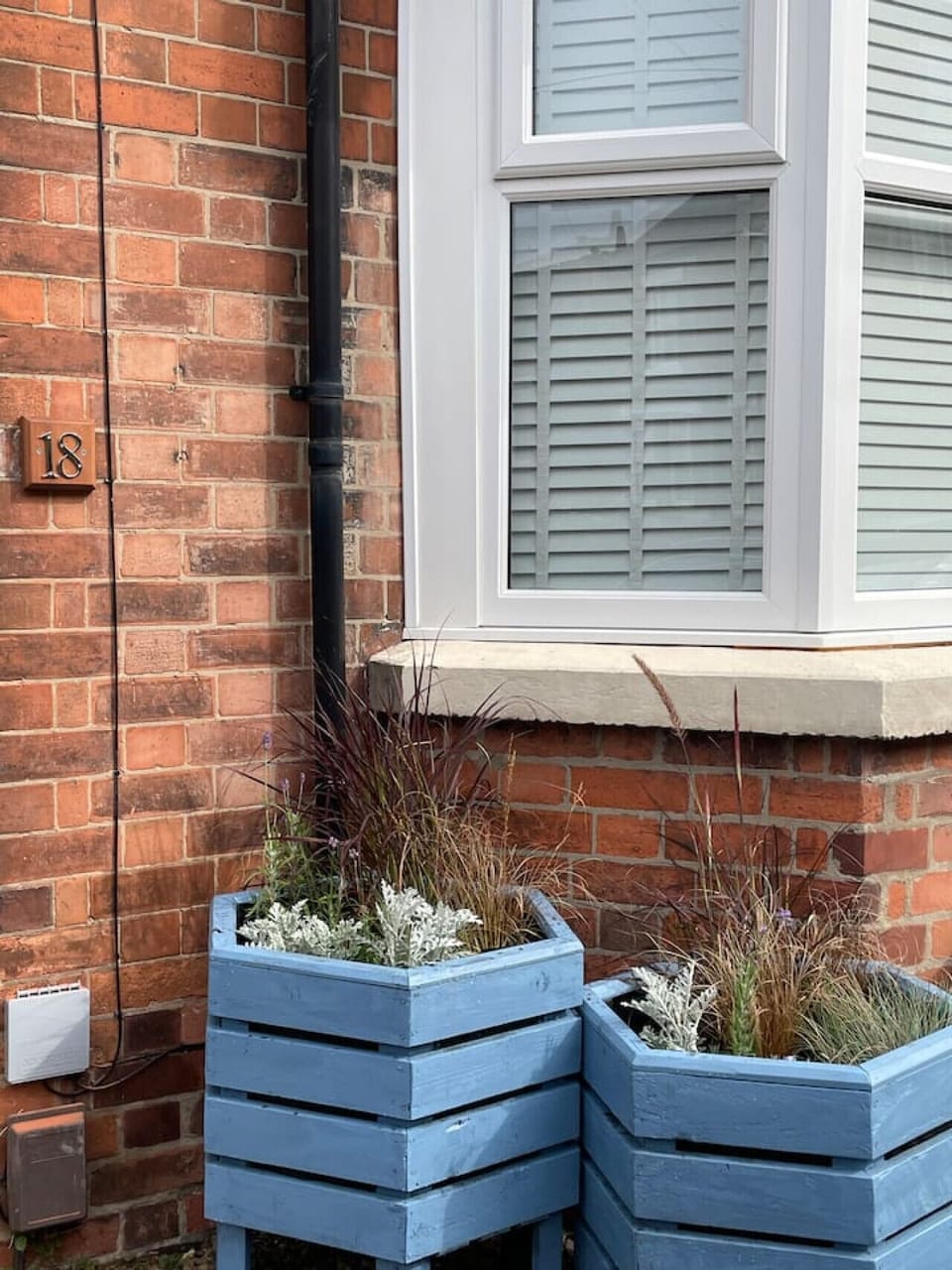 Exterior detail showing painted blue timber planters with ornamental grasses and seasonal planting against the red-brick front of the property.