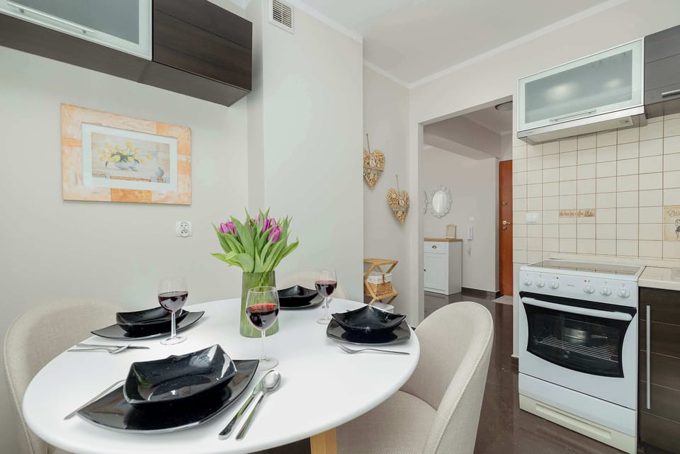 The dining space is centered around a round white table set with elegant black tableware and a fresh bouquet of tulips, creating a welcoming atmosphere.