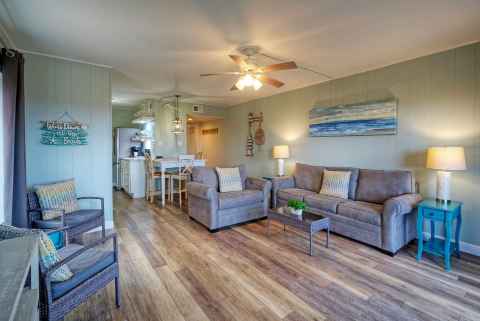 Bright coastal living area with plush seating, wood-look floors, and balcony access for fresh Gulf breezes.