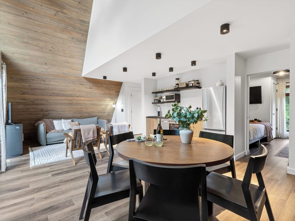 Vaulted A-frame great room with dining for 6, cozy lounge seating, and forest views through floor-to-ceiling windows.