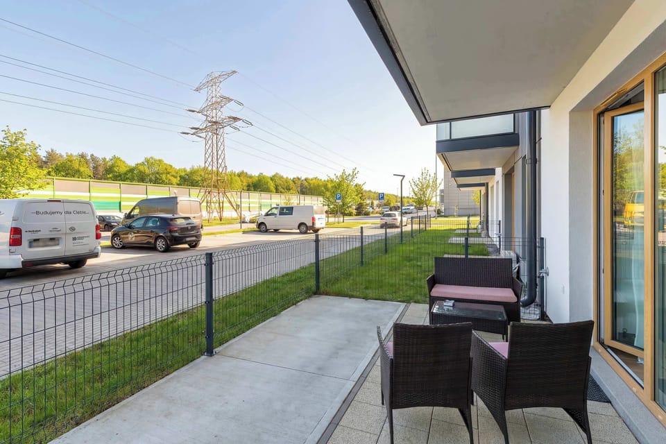 A private ground-floor terrace is equipped with dark wicker garden furniture and a small table. It offers an outdoor space to enjoy fresh air, separated by a low fence from the walkway.