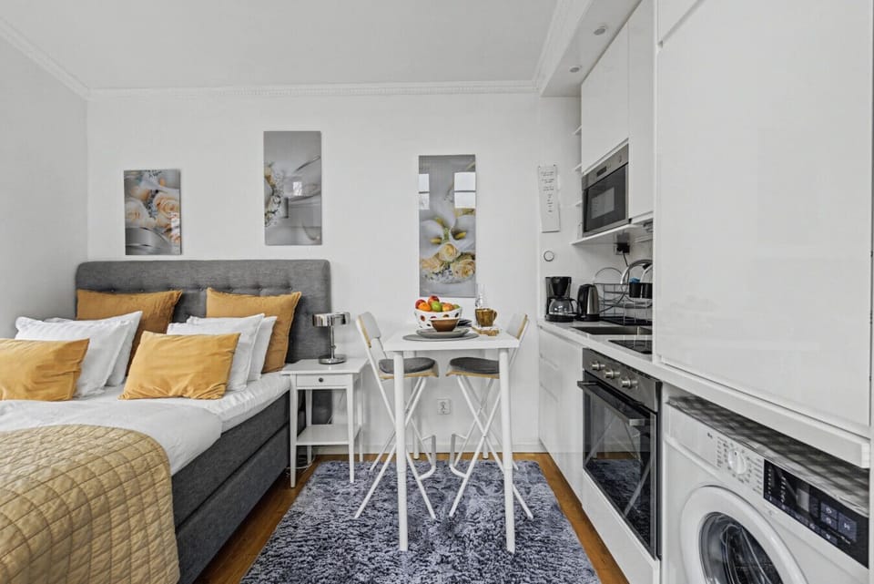 Open-plan studio layout with dining table for two and a well-equipped kitchenette featuring oven, stovetop, microwave, coffee maker, and in-unit washer.