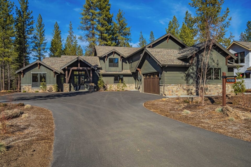 A stunning mountain lodge nestled among towering pines, featuring natural stone and timber architecture with a private driveway and garage.