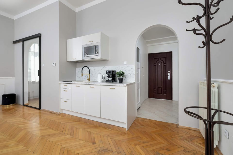 A hallway and entryway view showing a coat rack and the entrance to the kitchen area. The warm wood flooring continues through the archway, connecting the different spaces.