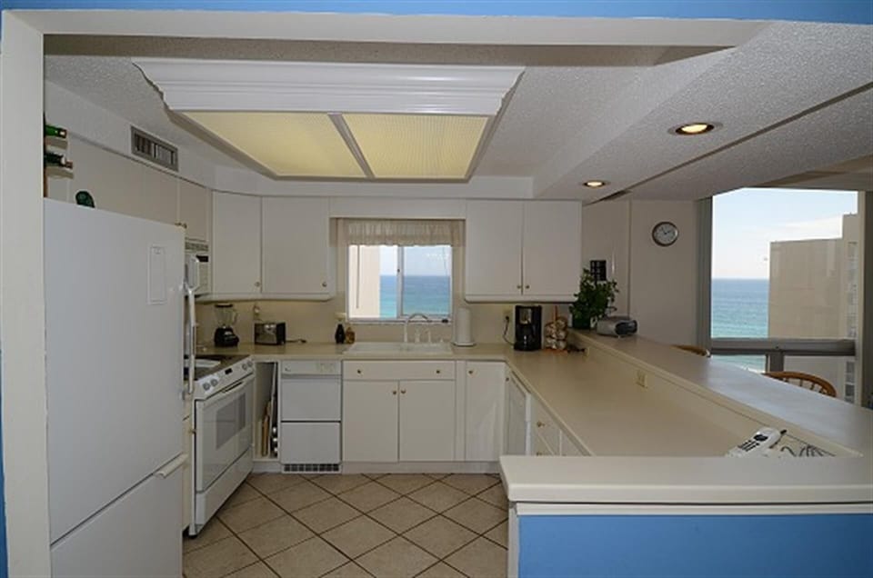 Cook with breathtaking ocean views streaming through your kitchen window, where white cabinets and warm lighting create the perfect coastal retreat.