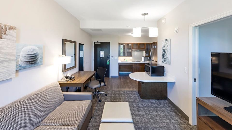 Framed artwork, a sofa, and a work desk with chair are positioned near a window that allows natural light into the living space.