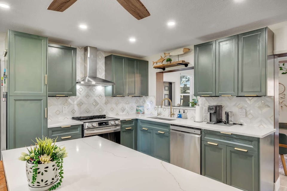 Modern kitchen with green cabinetry, stainless steel appliances, and a spacious white countertop island.