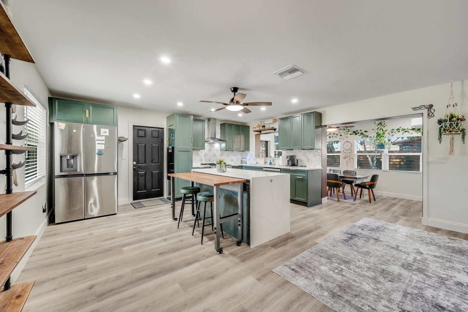 Modern kitchen with green cabinetry and a central island featuring a wooden breakfast bar.