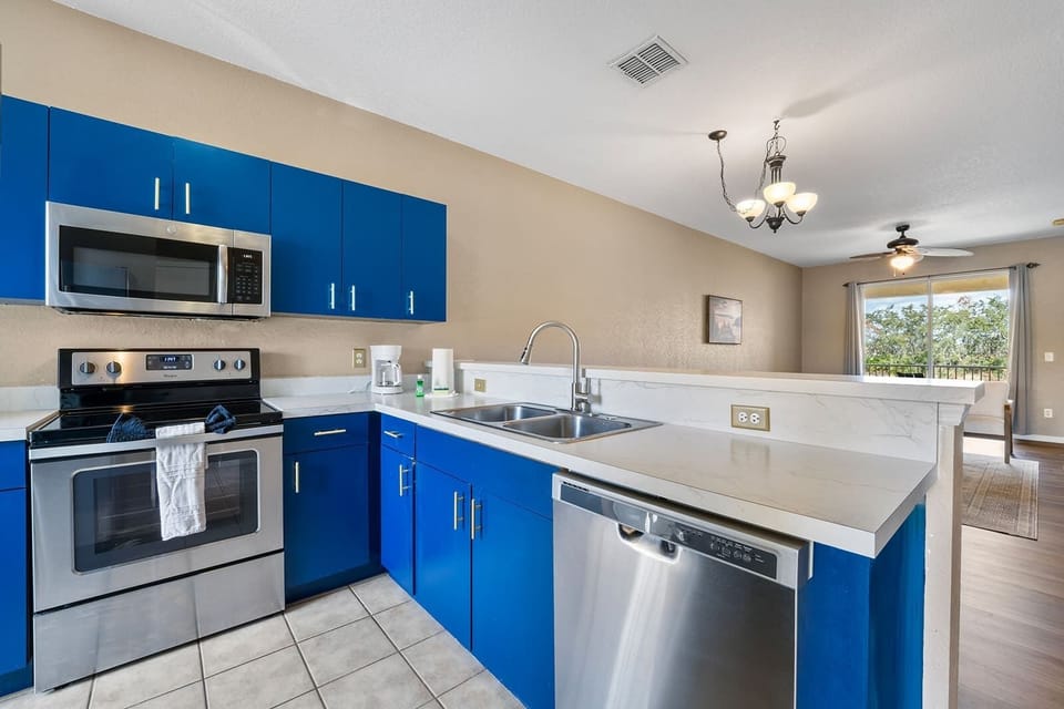 Modern kitchen with blue cabinetry and stainless steel appliances overlooking the living area.