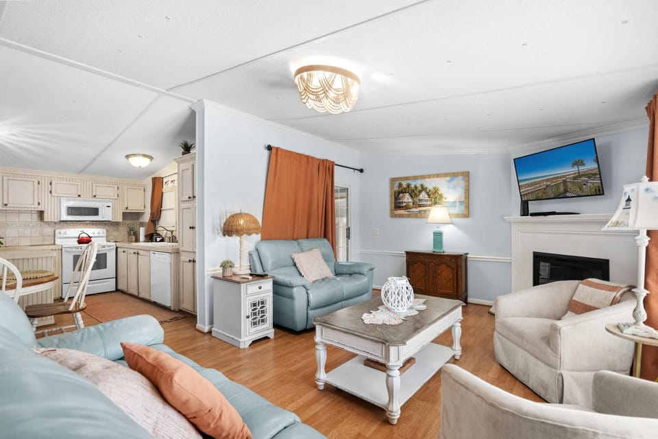 Living room with light blue leather sofas, beige armchairs, white distressed coffee table, and wall-mounted TV above fireplace.