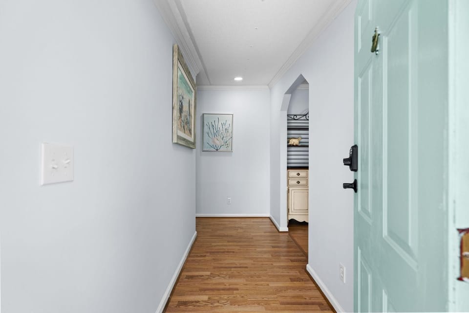 Entryway with light blue door, hardwood floors, soft gray walls, and coastal-themed artwork.